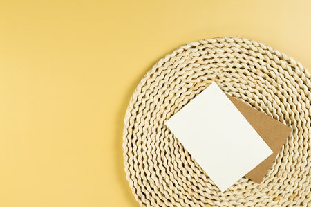 Top view of brown wicker table mat, white and brown cards on yellow background. Straw round tray, flat lay, copy space.の写真素材