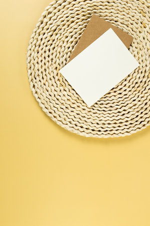 Top view of brown wicker table mat, white and brown cards on yellow background. Straw round tray, flat lay, copy space.の写真素材