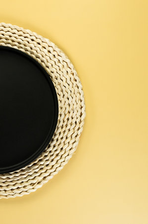 Top view of brown wicker table mat, black plate on yellow background. Straw round tray, flat lay, copy space.の写真素材