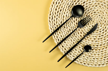 Top view of brown wicker table mat, black cutlery on yellow background. Straw round tray, flat lay, copy space.の写真素材