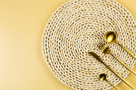 Top view of brown wicker table mat, gold cutlery on yellow background. Straw round tray, flat lay, copy space.の写真素材