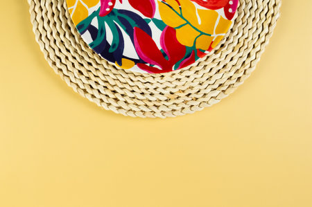 Top view of brown wicker table mat, colorful plate on yellow background. Straw round tray, exotic...