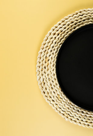 Top view of brown wicker table mat, black plate on yellow background. Straw round tray, flat lay, copy space.の写真素材