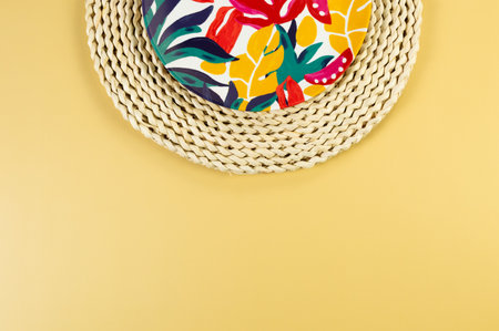 Top view of brown wicker table mat, colorful plate on yellow background. Straw round tray, exotic...