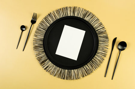 Top view of black wicker table mat, black cutlery, white card on yellow background. Straw round tray, flat lay, copy space.の写真素材