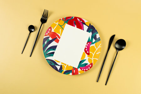 Top view of colorful plate, white card, black cutlery on yellow background. Exotic plant plate, summer picnic. Flat lay, copy space.の写真素材