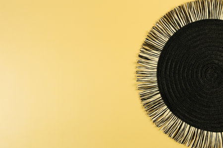 Top view of black wicker table mat on yellow background. Straw round tray, flat lay, copy space.の写真素材