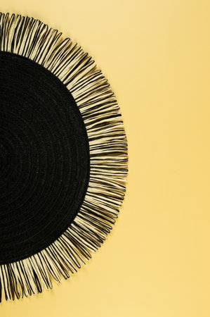 Top view of black wicker table mat on yellow background. Straw round tray, flat lay, copy space.
