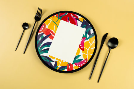 Top view of black tray, colorful plate, black cutlery on yellow background. White card, exotic plant plate, summer picnic. Flat lay, copy space.の写真素材