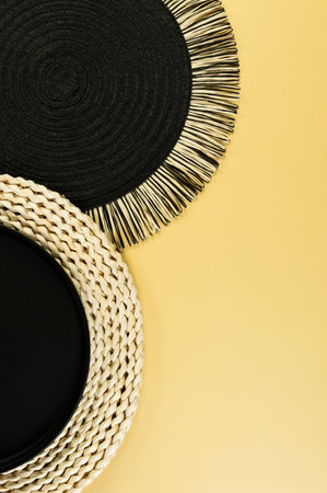 Top view of brown wicker table mat, black plate, black tray on yellow background. Straw round tray, flat lay, copy space.の写真素材