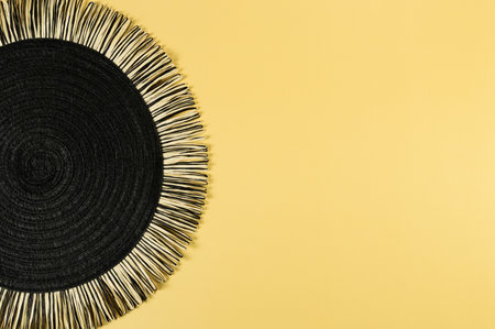 Top view of black wicker table mat on yellow background. Straw round tray, flat lay, copy space.の写真素材