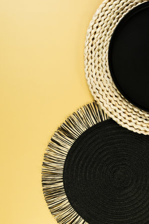 Top view of brown wicker table mat, black plate, black tray on yellow background. Straw round tray, flat lay, copy space.の写真素材