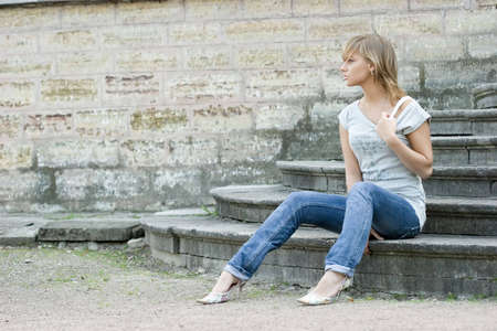 Young beautifull girl sitting on vintage footsteps with closed eyes near old grungy wall. の写真素材