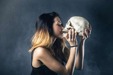 Woman kissing skull against dark backgroundの写真素材