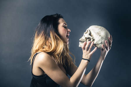 Woman kissing skull against dark backgroundの写真素材