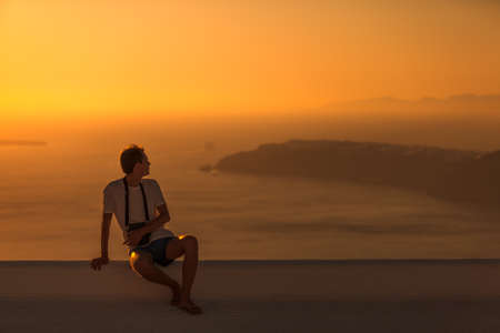 Man sitting on the roof at sunset. Beautiful view on caldera at evening sun. Imerovigli, Santorini island, Greeceの写真素材