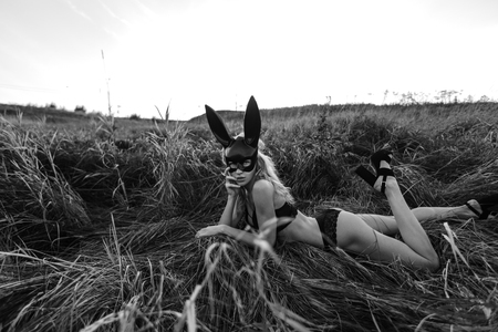 Beautiful sexy woman wearing black fashion bunny mask laying in grass at the field.の写真素材