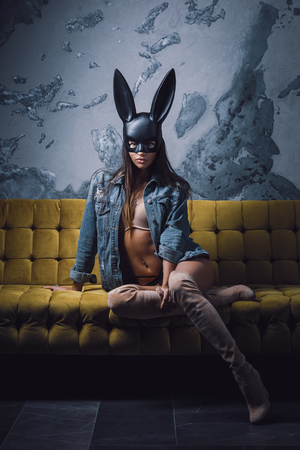 Sexy fashion model sitting on sofa in black rabbit maskの写真素材