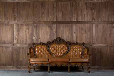 Vintage leather sofa with carved elements standing near the wooden wall.の写真素材