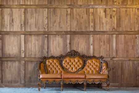 Vintage leather sofa with carved elements standing near the wooden wall.の写真素材