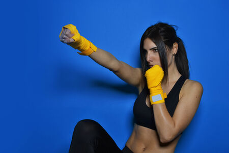 beautiful fitness woman with the yellow boxing bandage against the blue backgroundの写真素材