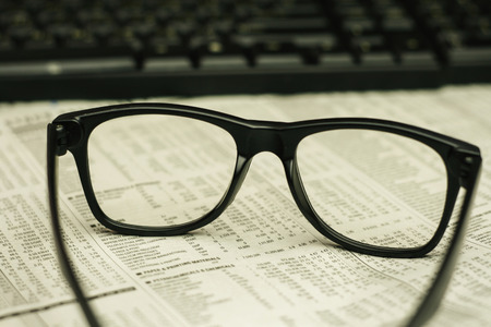 keyboard and a black eyeglasses on a financial newspaper with a very shallow depth of field with copy space for textの写真素材