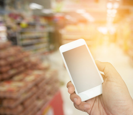 hand holding the smartphone on supermarket in blurry for background with burst lightの写真素材