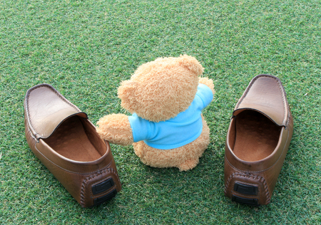 Teddy bear sitting on the green grass with brown shoes . Concept about travelの写真素材