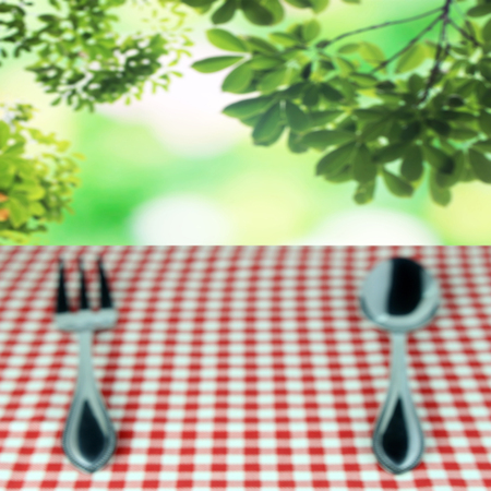 blur spoon with fork on checkered tablecloth and blur leaves background