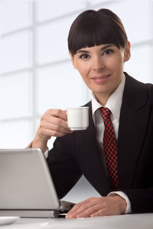 The business woman with a coffee cup in a hand, sits at a computerの写真素材