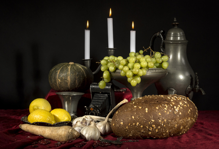 Dutch still life with grapes and candle and old camera and red draperies on a dark black backgroundの写真素材