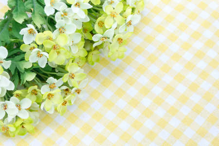 Plastic flowers decorations on a yellow tablecloth backgroundの写真素材