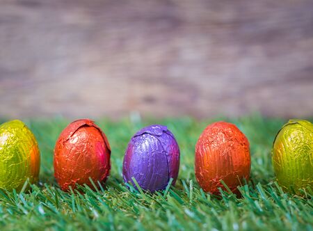 Raw of Chocolate Easter Eggs over grass with wooden background