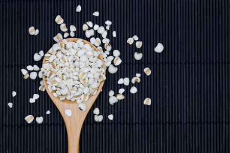 Millet rice, Adlay in wooden spoon on the black bamboo mat background, Selective focusの写真素材