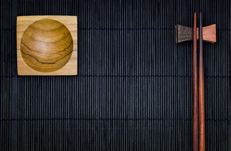 Wooden Sauce bowl and chopsticks on the black bamboo mat background in top viewの写真素材