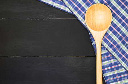 Wooden spoon over plaid tartan tablecloth on black wooden table in top viewの写真素材