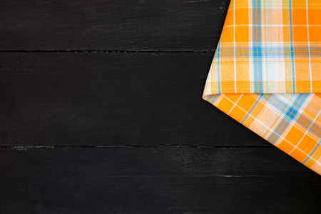 The plaid tartan tablecloth on black wooden table in top view