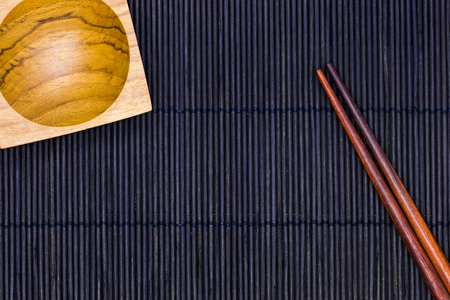 Wooden Sauce bowl and chopsticks on the black bamboo mat background in top viewの写真素材