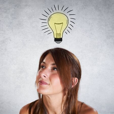 Portrait of smiling woman thinking with bulb on grey backgroundの写真素材