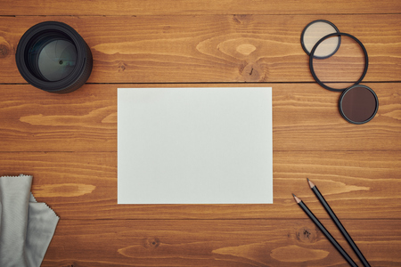 White paper and pencil on wooden table with camera lensの写真素材