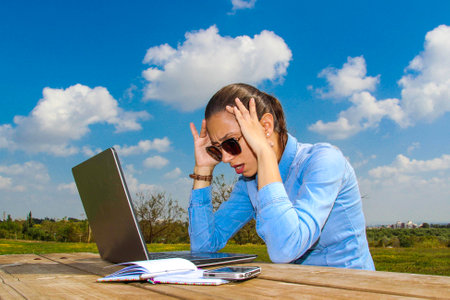 A women with laptop, sitting in the garden, Holding your head because of problems at workの写真素材