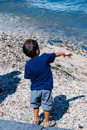 Little boy standing on the pebble beach and pointing at somethingの写真素材