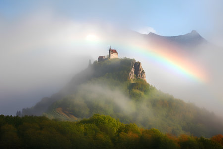 Old castle on top of the mountain in foggy morning with rainbowの素材