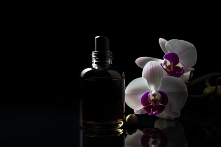 Bottle of essential oil and orchid flowers on a black backgroundの素材