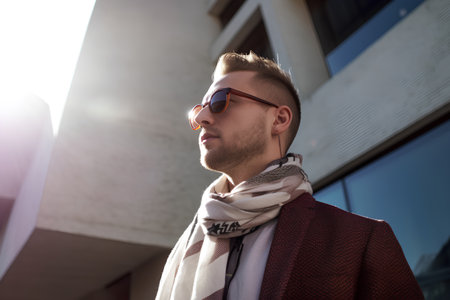 Young handsome man in a coat, scarf and sunglasses on the streetの素材