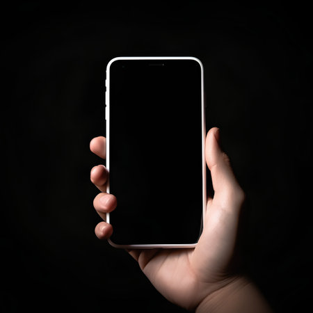 male hand holding a white smartphone with black screen isolated on black backgroundの素材