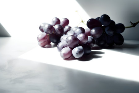 bunch of purple grapes on a white table with light and shadowの素材