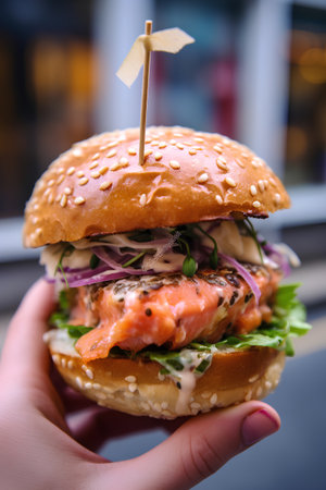 Closeup of female hand holding hamburger with salmon, onion and cheeseの素材