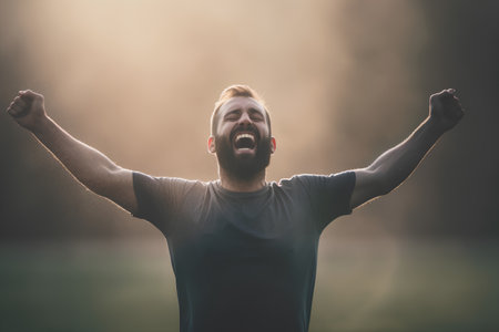 Young happy man celebrating success with arms raised in the air on a sunny dayの素材
