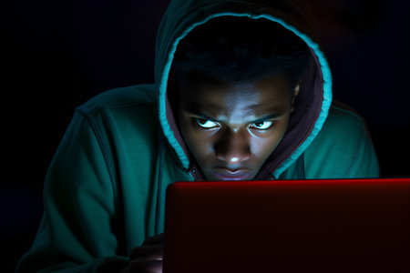 Young man in hoodie using laptop computer in dark room. Cyber attack concept.の素材